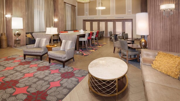 Een ruime hotel lobby met een groot eetgedeelte, diverse zithoeken en een decoratief vloerkleed.