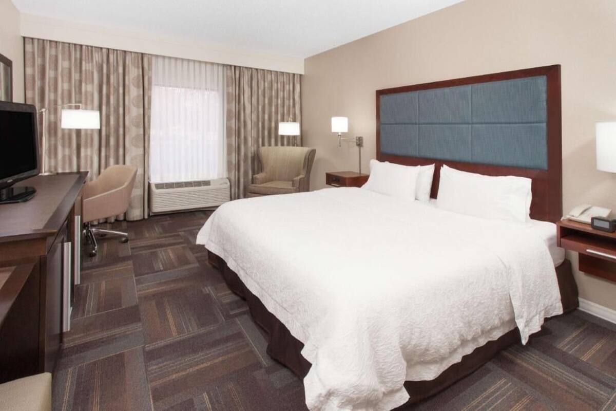 Une chambre d’hôtel avec un grand lit, un bureau avec une chaise, une télévision et une fenêtre avec des rideaux.