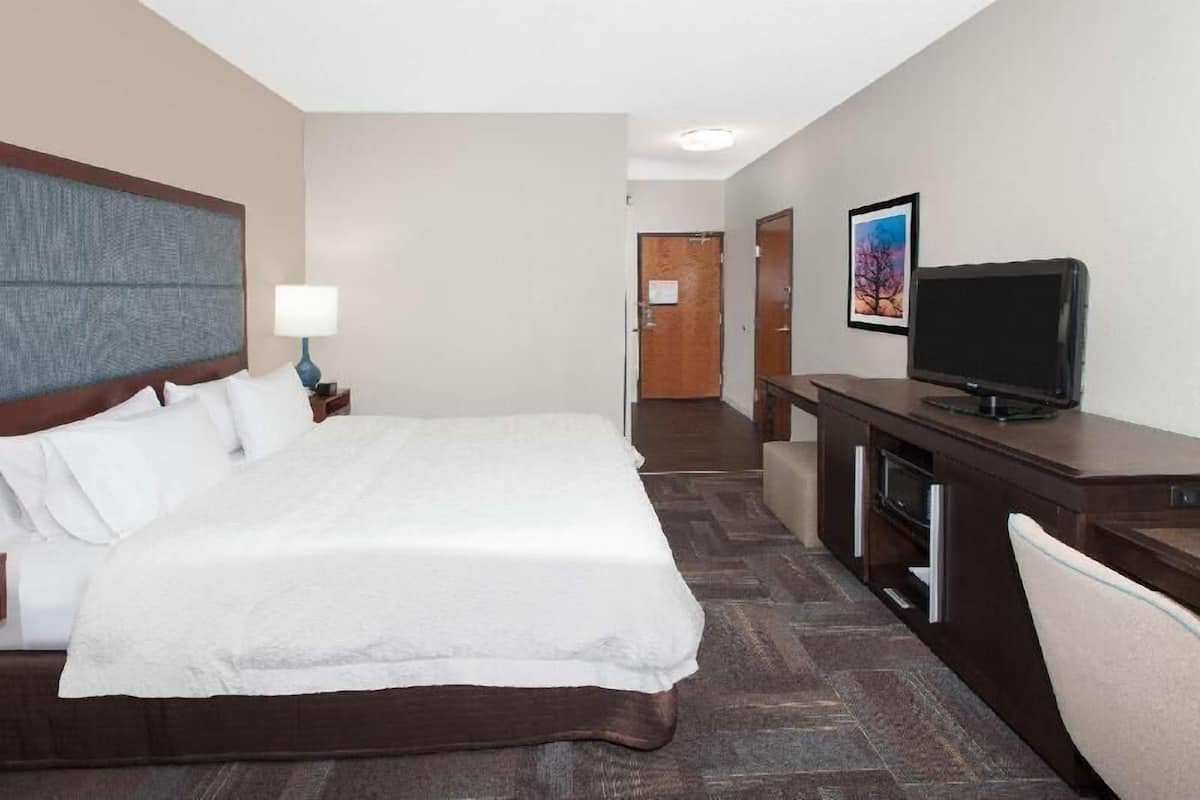 Une chambre d’hôtel avec un grand lit, un bureau avec une télévision et une porte donnant sur une autre pièce.