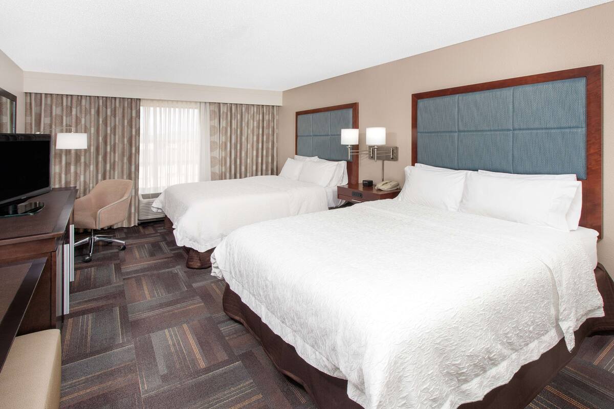 Une chambre d’hôtel avec deux lits, un bureau avec une télévision et une chaise.
