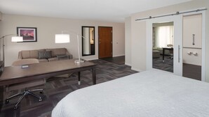 Een hotelkamer met een groot bed, een bureau met stoel, een bank, een spiegel en een deur naar een andere kamer.