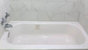 A bathroom with white marble tiles and a white bathtub. - Sunrise Inn (Bradenton)