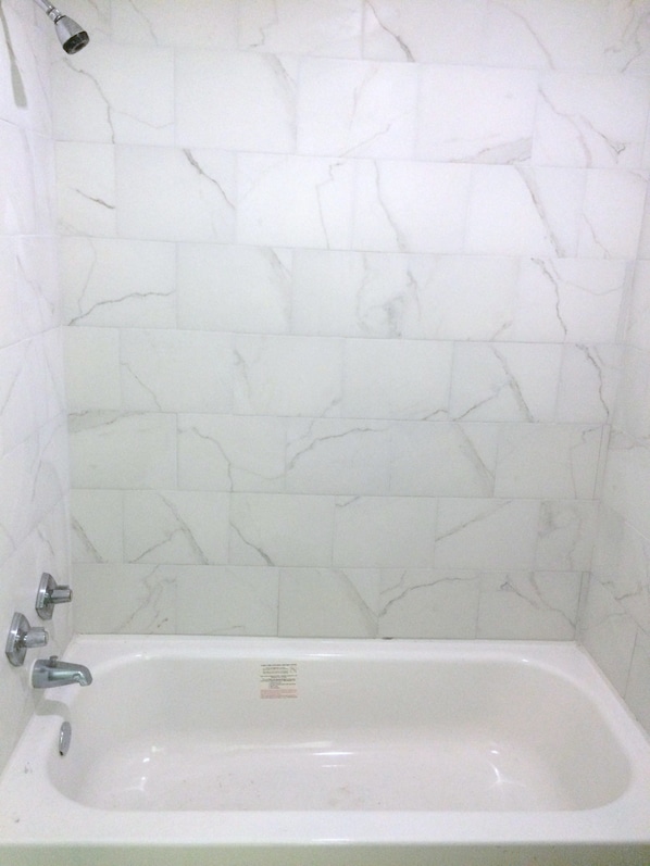Ein Badezimmer mit weißen Marmorfliesen und einer weißen Badewanne.