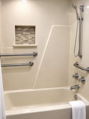 A bathroom with a bathtub, grab bars, a showerhead, and a towel rack. - Sunrise Inn (Bradenton)