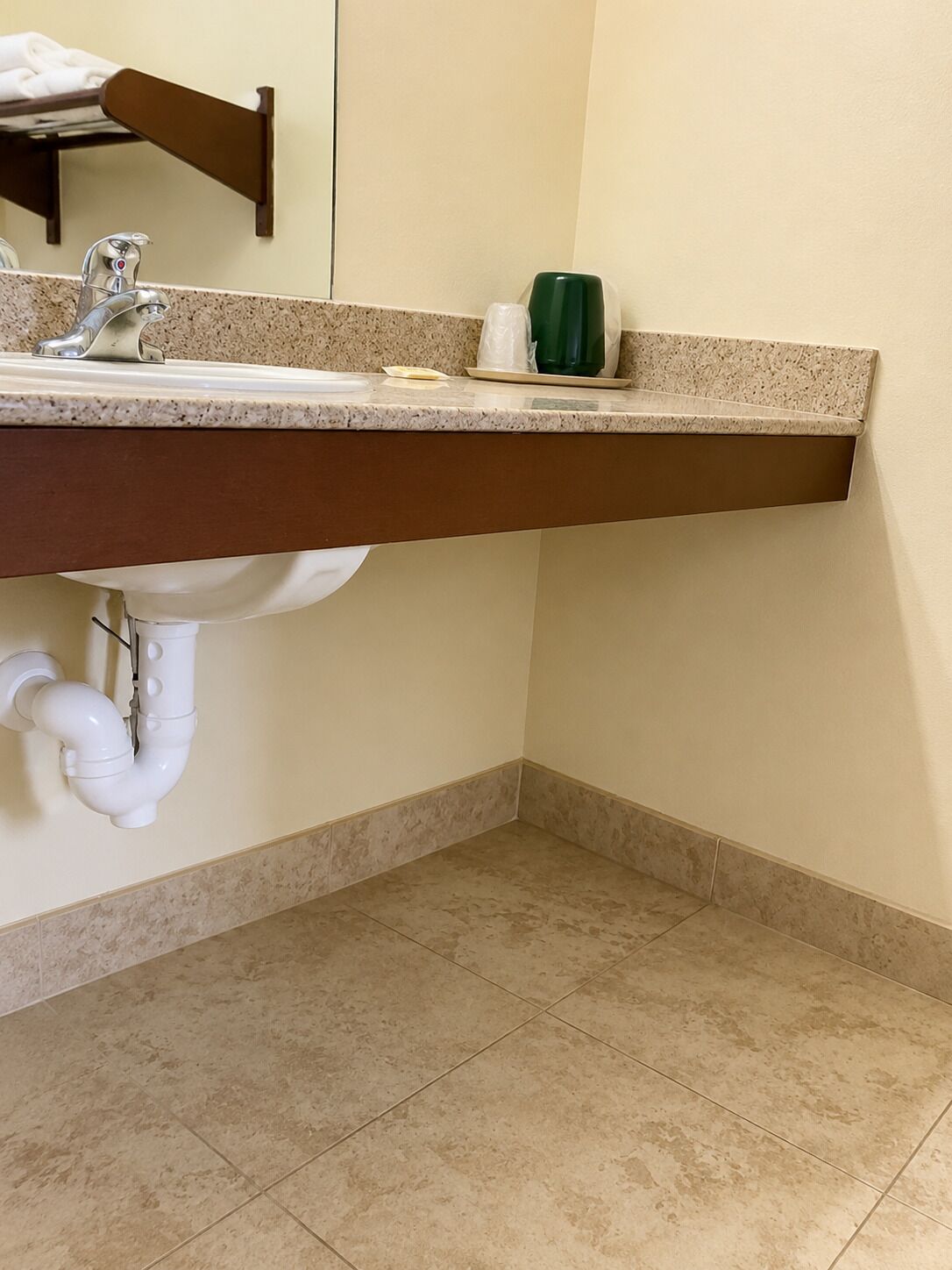 Une salle de bain avec un lavabo, un miroir, un porte-serviettes et une bouteille verte posée sur le comptoir.