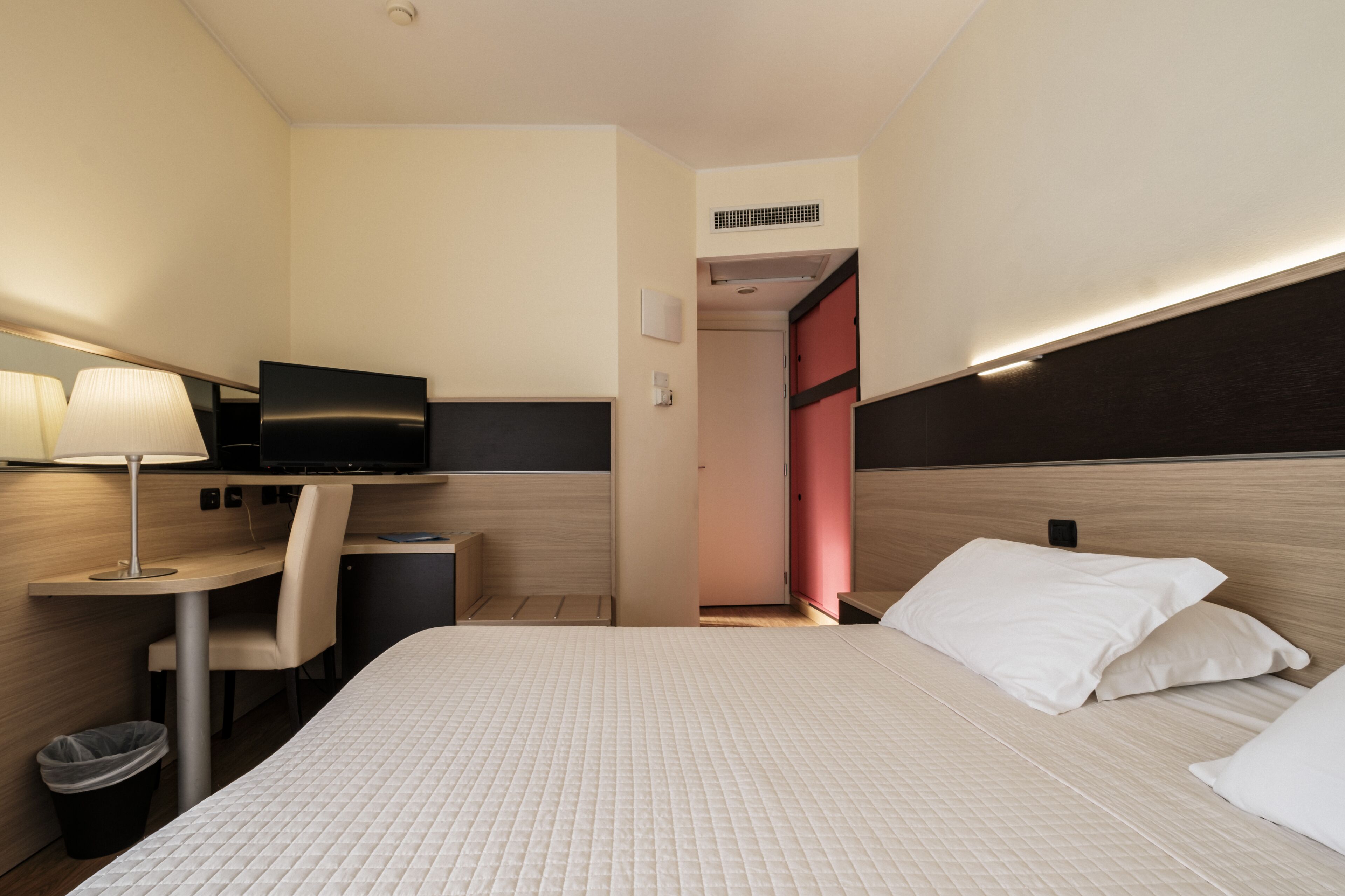 Una habitación de hotel con cama, escritorio, silla, televisión y un cubo de basura.