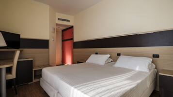 A hotel room with a bed, desk, chair, and a small table.