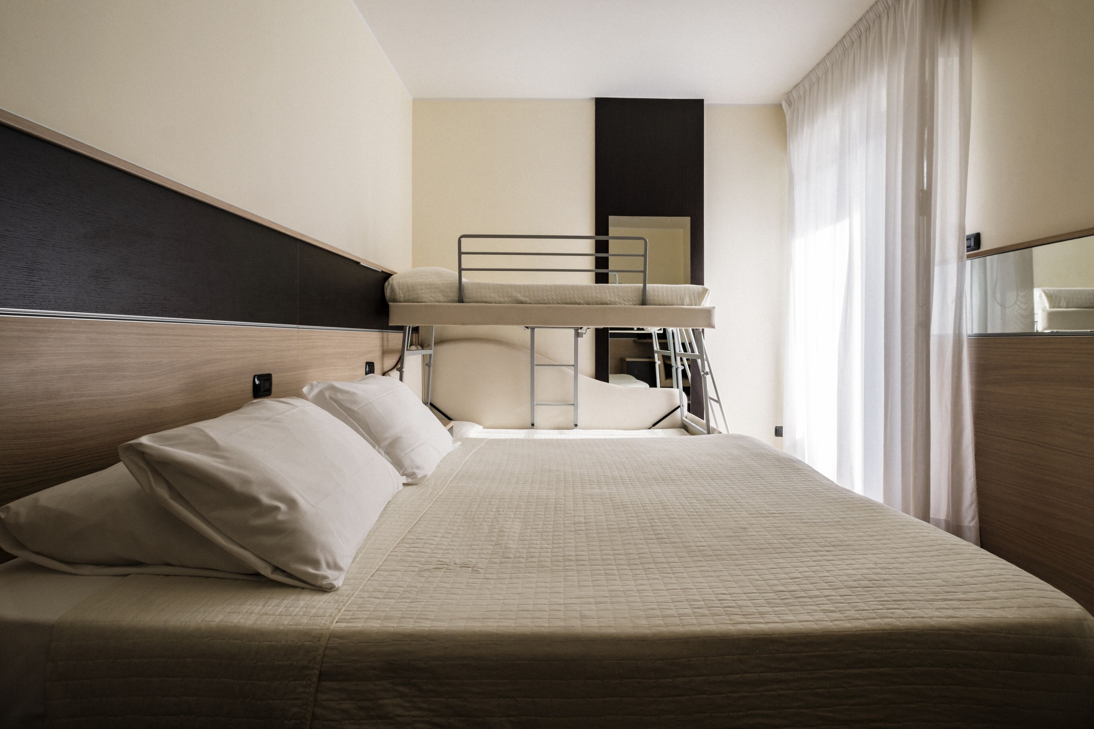 A hotel room with a bunk bed, a single bed, and a large window with curtains.