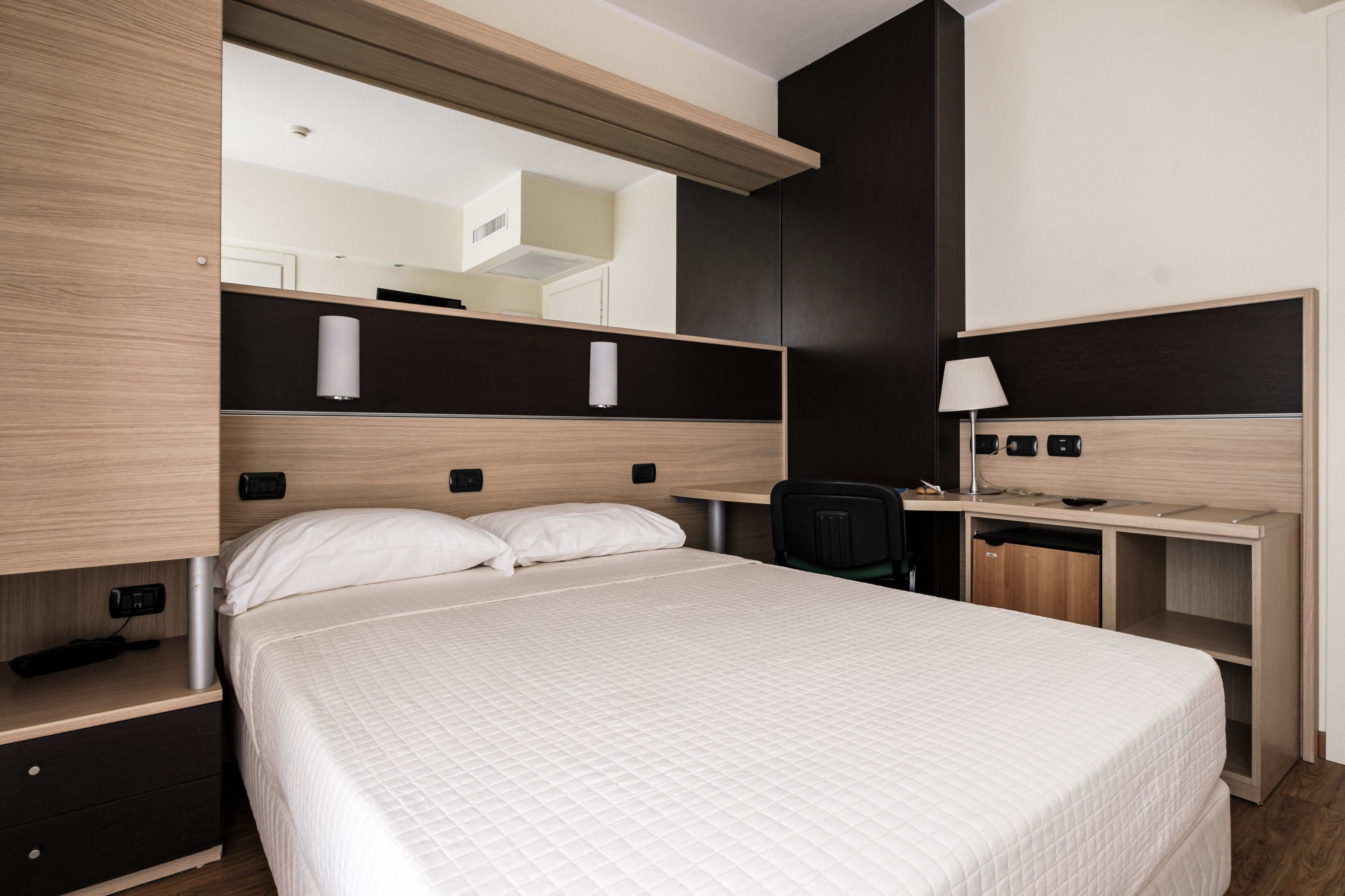 Moderni hotellihuone, jossa on suuri sänky, työpöytä ja peili.