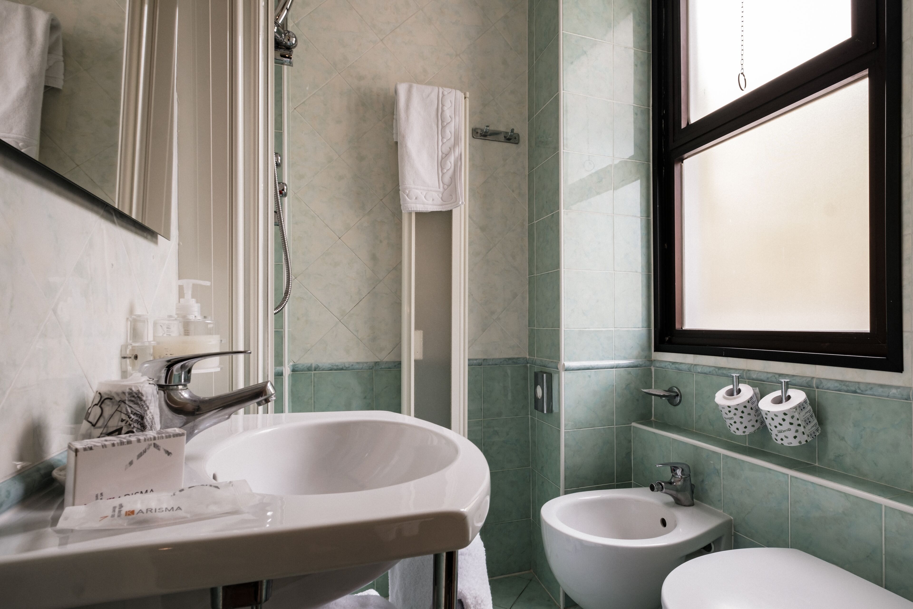 A bathroom with a sink, bidet, and a window.