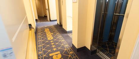 Un pasillo de hotel con alfombra estampada, barandilla y una puerta con un letrero.