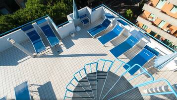 A rooftop pool area with multiple sun loungers and a staircase leading to an upper level.