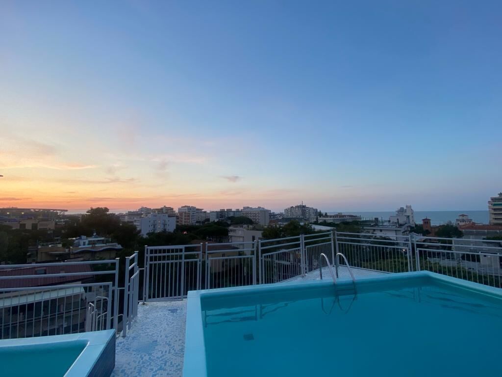 Piscina no terraço com vista para a cidade ao pôr do sol.