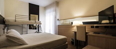 A hotel room with a bed, a desk, a chair, a TV, and a lamp.