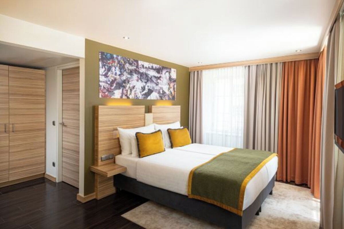 A modern bedroom with a large bed, wooden wardrobe, and a painting on the wall.