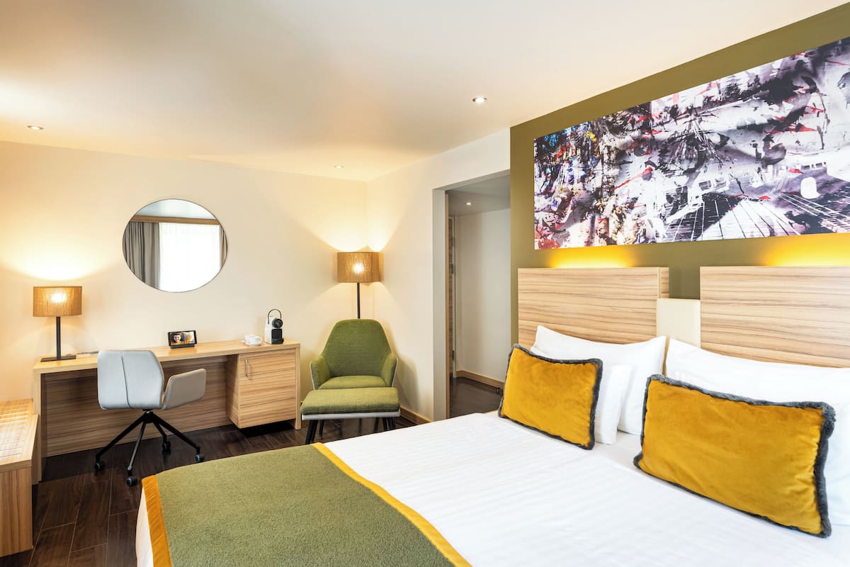 A hotel room with a bed, desk, chair, and a large painting on the wall.