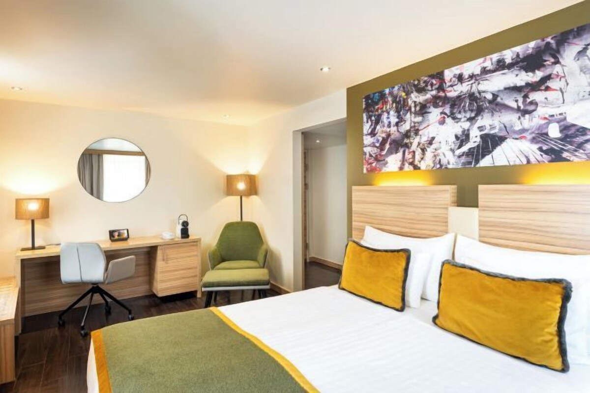Habitación de hotel con cama, escritorio, silla y un cuadro abstracto grande en la pared.