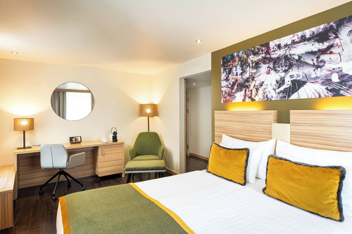 Ett hotellrum med en säng, ett skrivbord, en stol och en stor tavla på väggen.