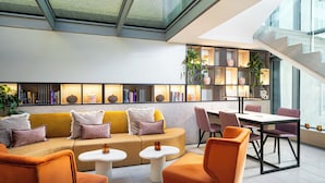 A modern lounge area with a sofa, chairs, and a table, featuring bookshelves and plants. -  Leonardo Boutique Hotel Salzburg Gablerbräu (Salzburg)