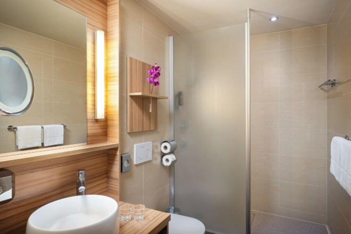 A modern bathroom with a large mirror, wooden vanity, white sink, and a glass-enclosed shower.