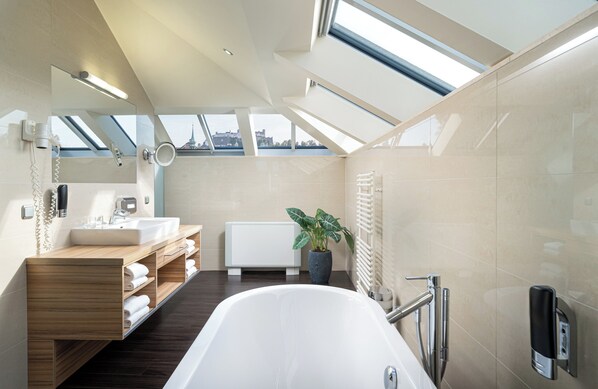 A modern bathroom with skylights, a bathtub, a sink, and a mirror.