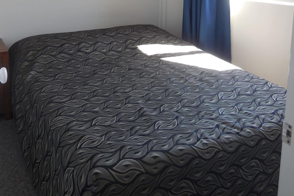 Een slaapkamer met een bed, een plafondventilator, een raam met blauwe gordijnen en een airconditioning op de muur.