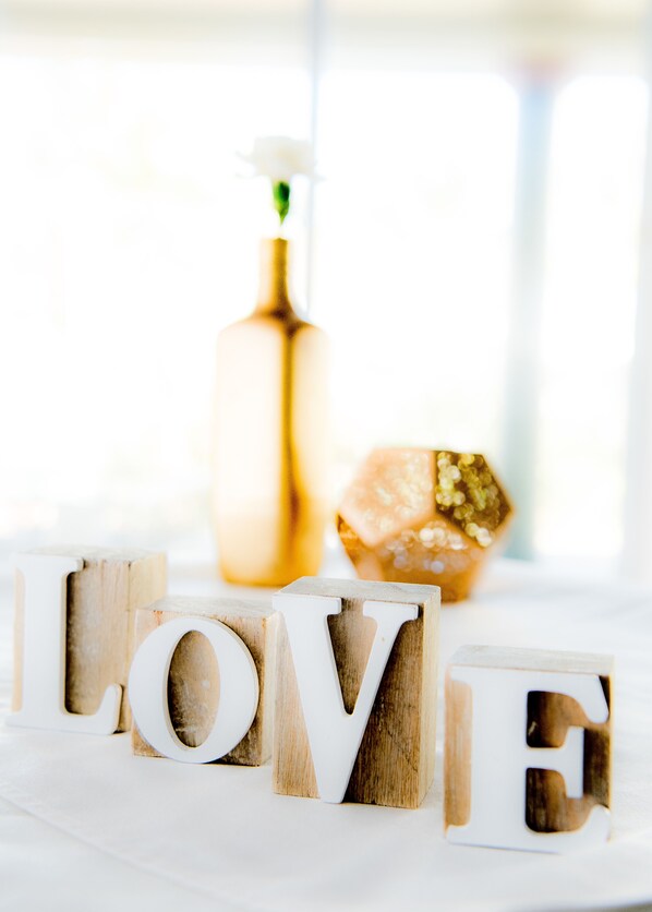 Bloques de madera que deletrean "LOVE", con una botella y un adorno de fondo.