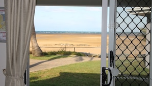 Vista a través de una puerta con cerca de malla, un área con césped y una playa arenosa al fondo.