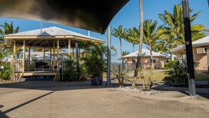 Un espacio al aire libre techado con un pabellón, palmeras y un edificio al fondo.