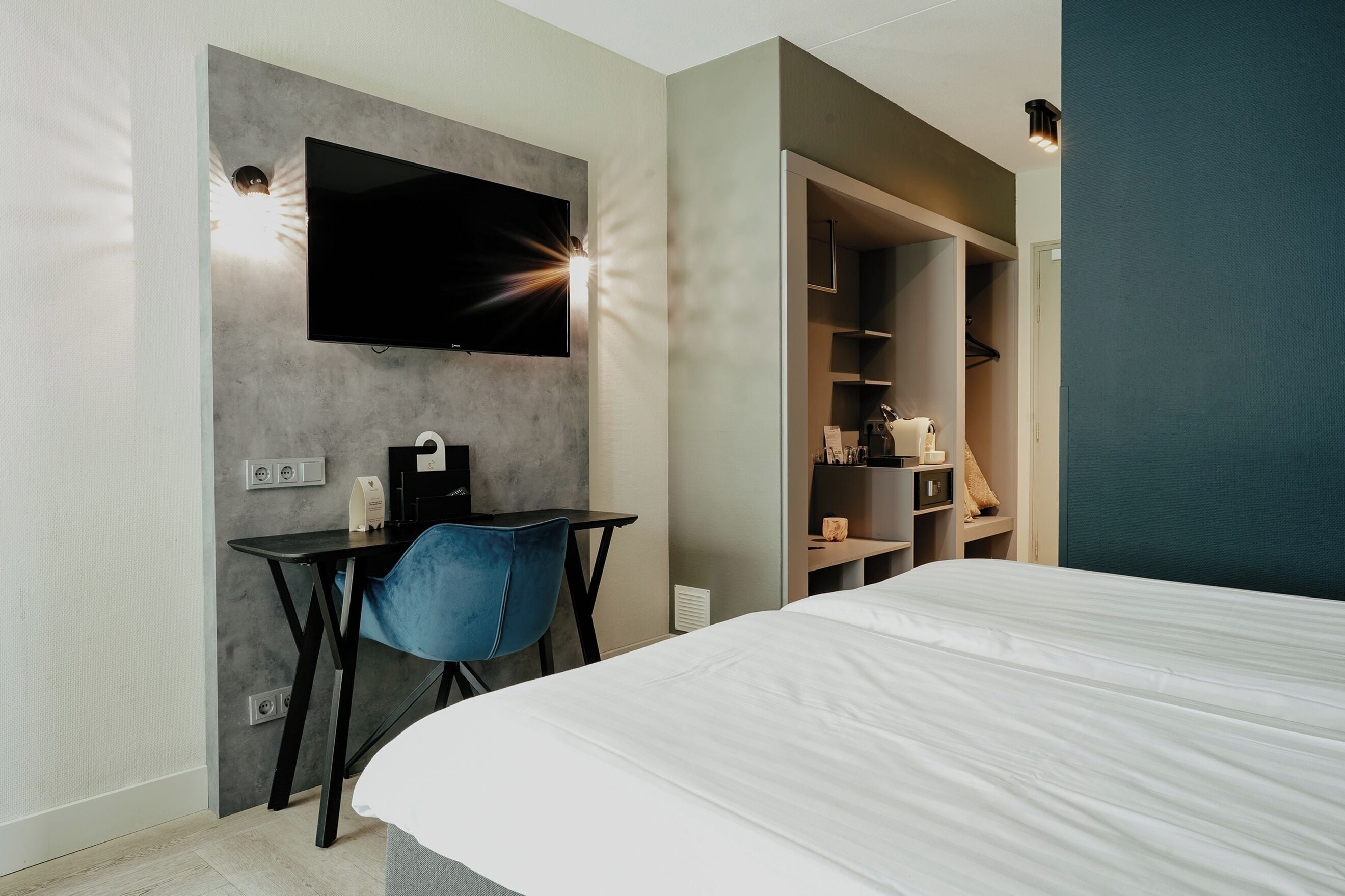 Una habitación de hotel moderna con una cama, un escritorio con una silla, un televisor montado en la pared y un vestidor.