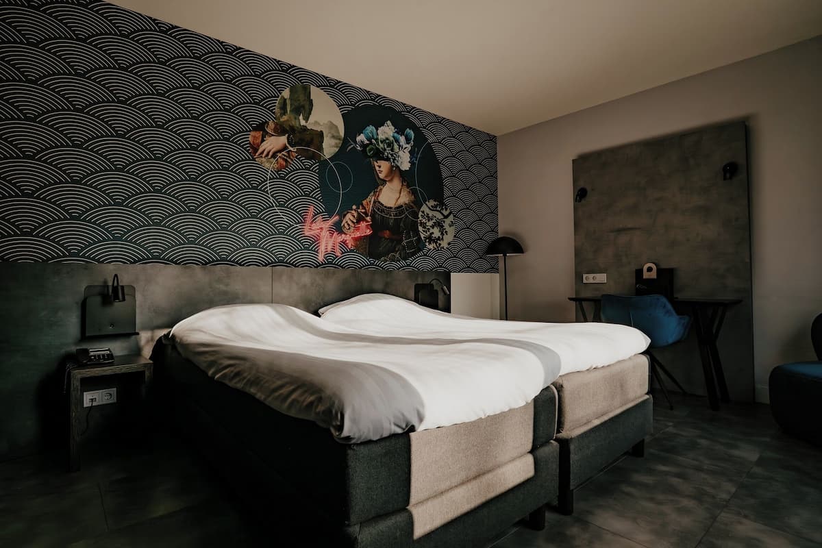 Ein modernes Schlafzimmer mit einem großen Bett, einem Nachttisch mit Lampe, einem Schreibtisch und einem Sessel.