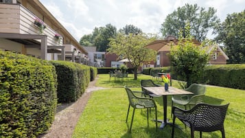 Un patio con una mesa y sillas, rodeado de setos y árboles.