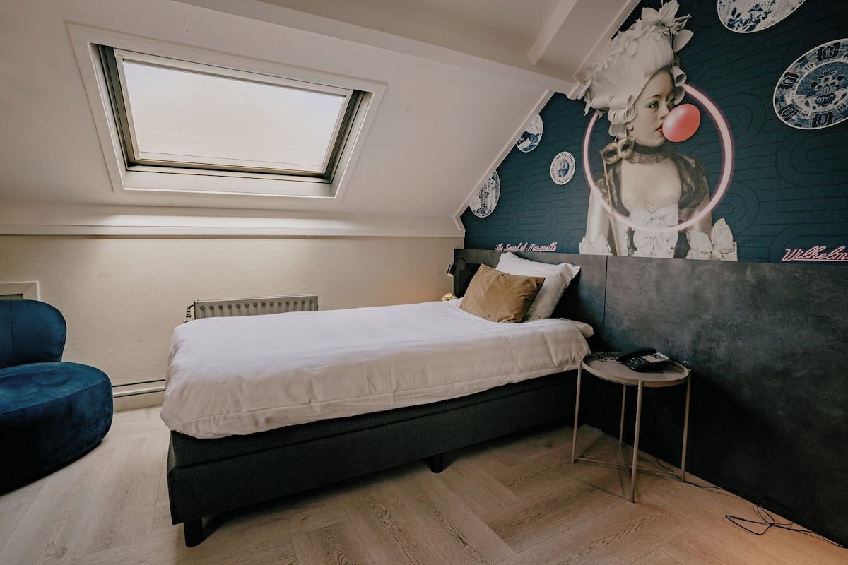 Ein Schlafzimmer mit Dachfenster, einem Bett mit Kissen, einem kleinen runden Tisch und einer Wand mit Wandmalerei.