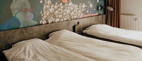 A hotel room with two beds, a large abstract painting on the wall, a radiator, and a black lamp.