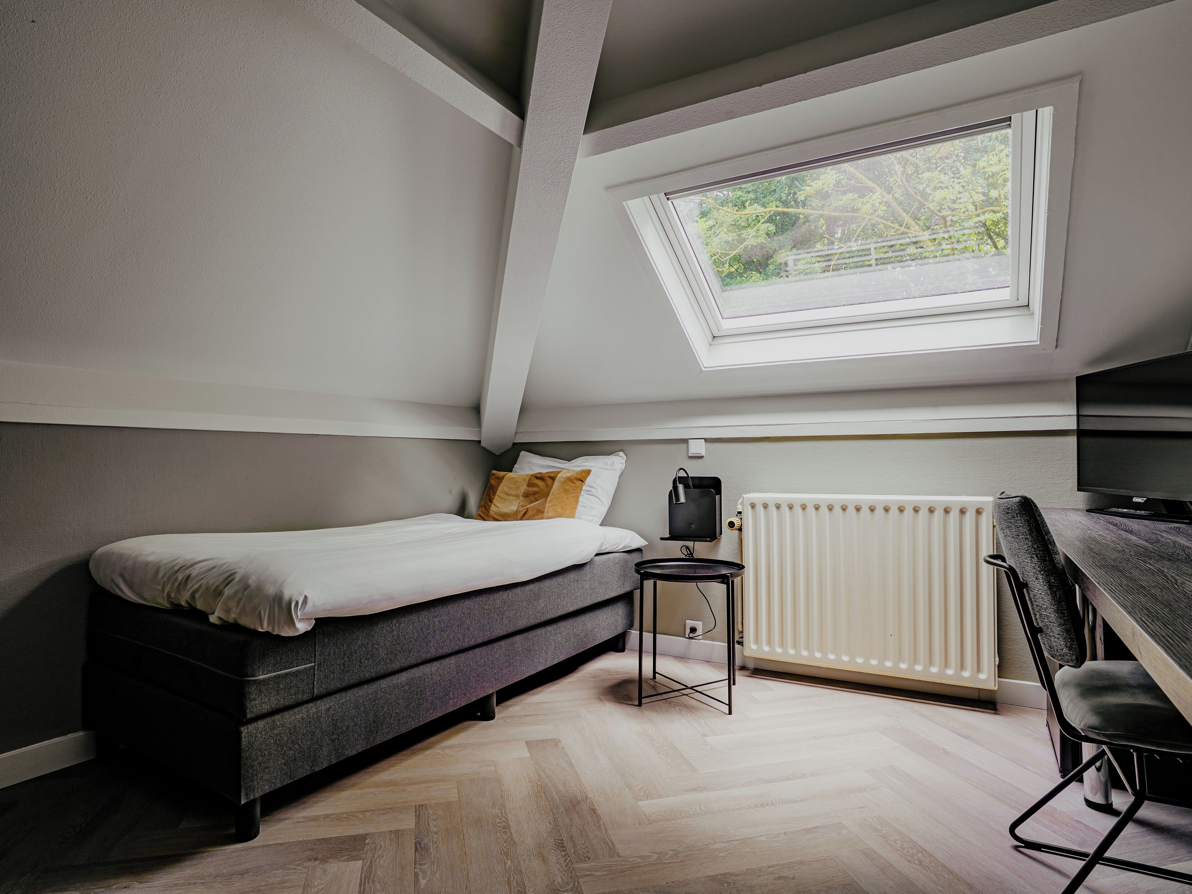 Une chambre compacte et moderne, dotée d’un lit en mezzanine, d’une petite table d’appoint, d’un radiateur et d’un téléviseur.