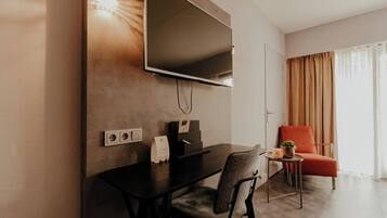 A modern room with a flat-screen TV mounted on the wall, a desk with a chair, a small table with a plant, and a red chair.