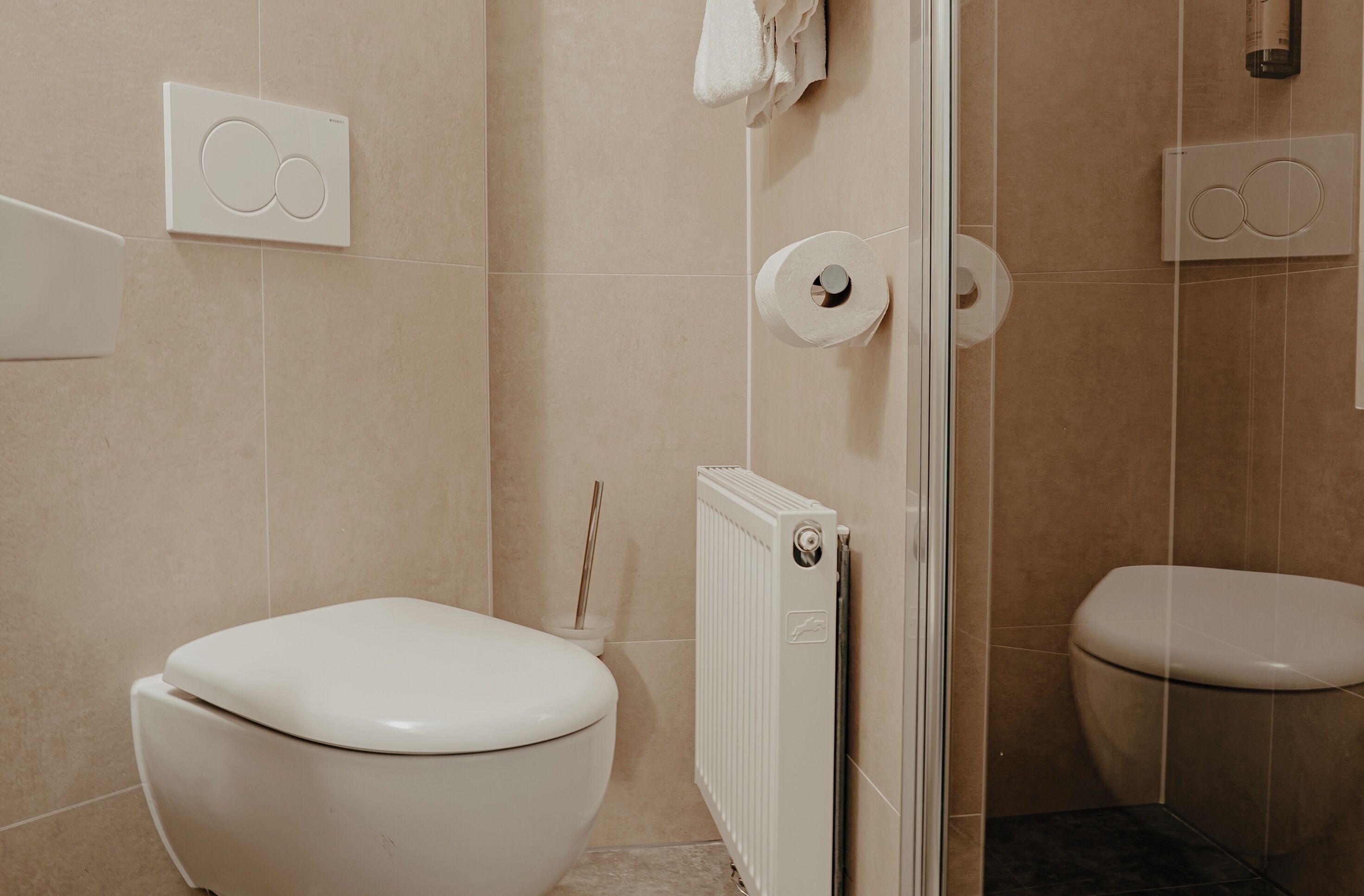 A modern bathroom with two toilets, a shower, and a towel rack.