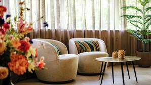 Une pièce avec deux fauteuils beiges, une petite table ronde aux pieds noirs et une plante en pot.