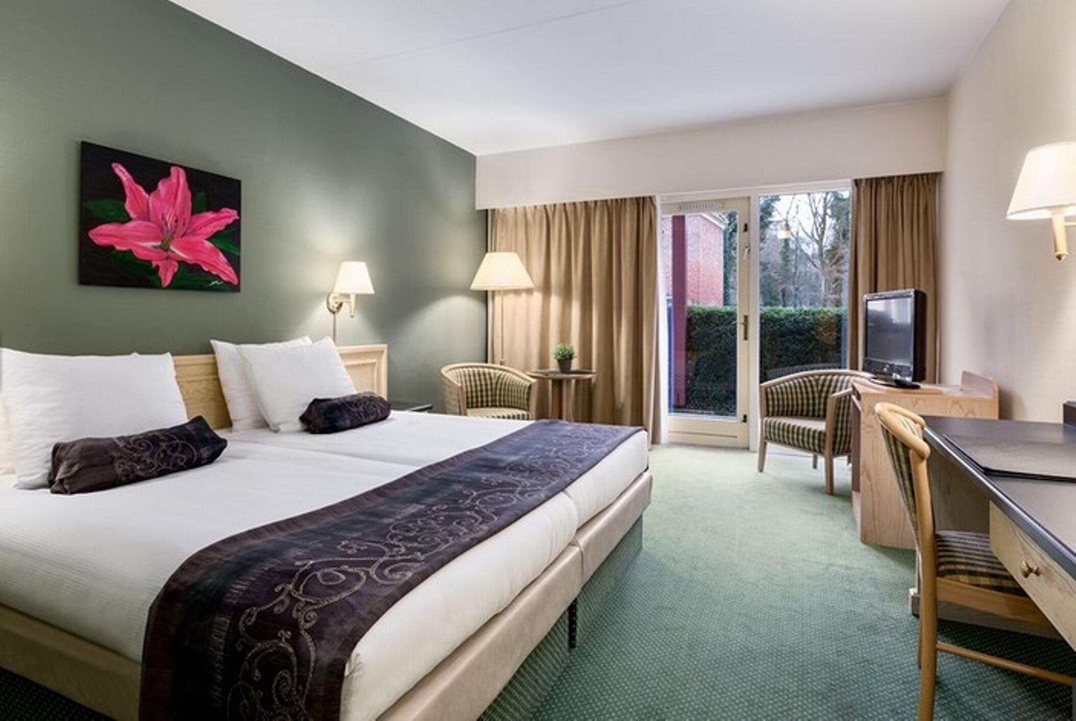 A hotel room with a bed, a desk, a chair, a TV, and a window with curtains.