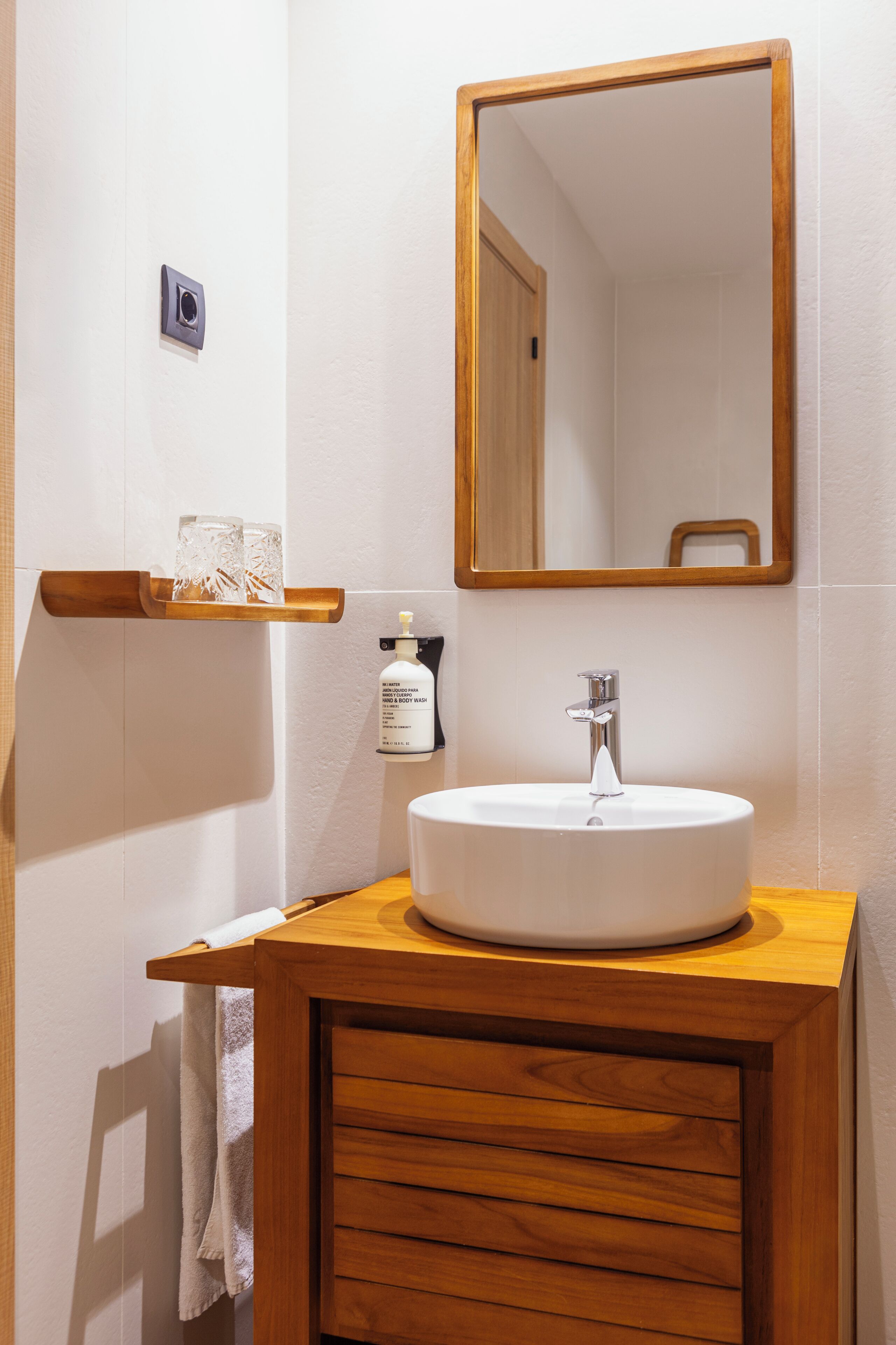Un baño con tocador de madera, lavamanos blanco, espejo y toallero.