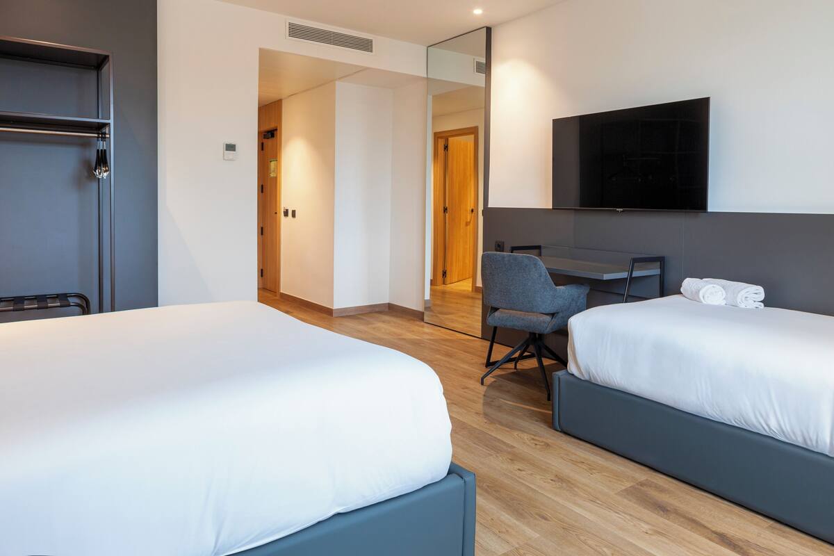 Ein Hotelzimmer mit zwei Betten, einem Schreibtisch, einem Stuhl, einem Fernseher und einem Spiegel.