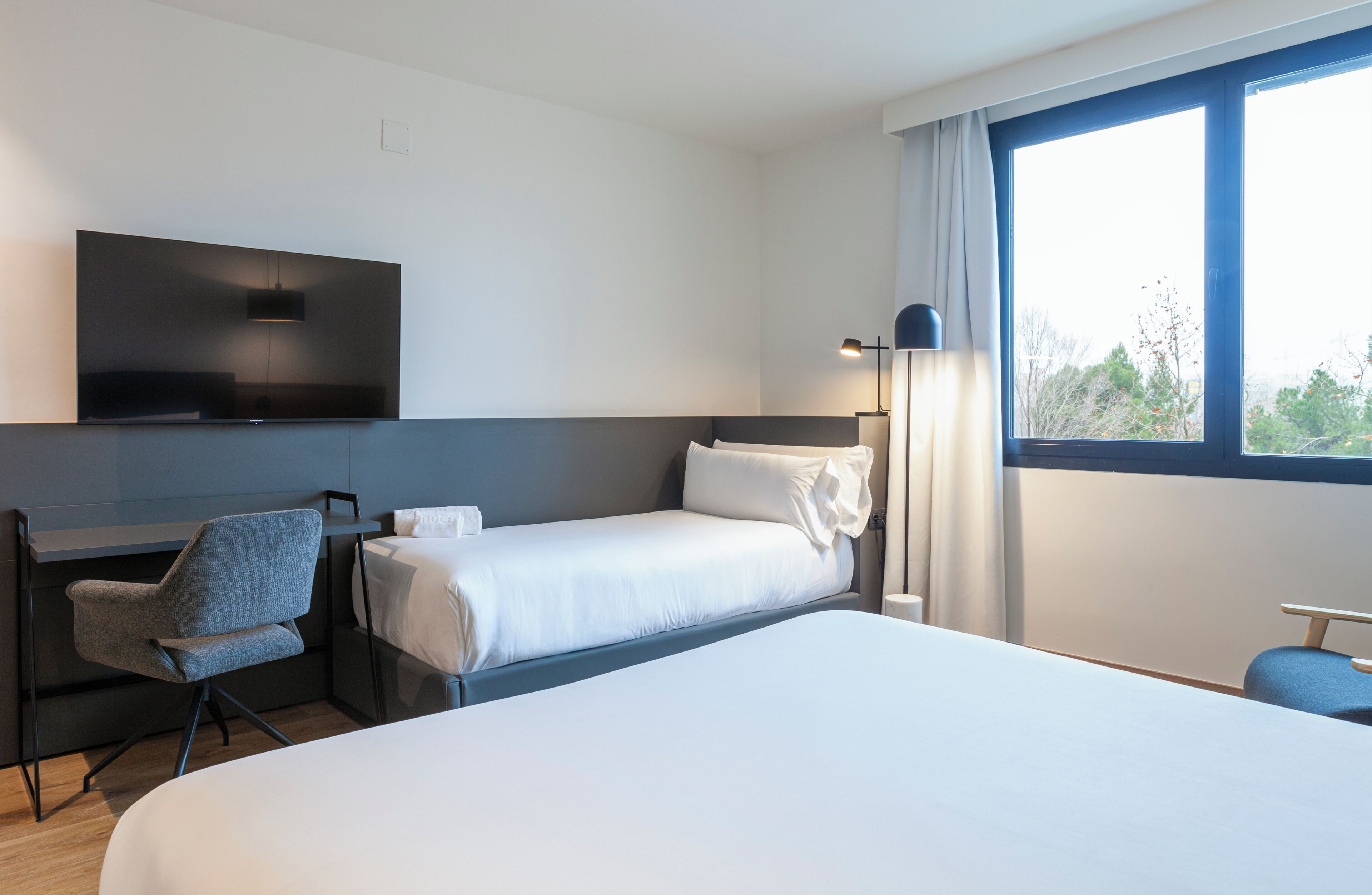 Una habitación de hotel con cama, escritorio, silla, televisión y ventana con vistas.