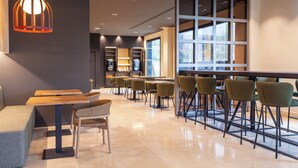 A modern cafe with wooden tables, green chairs, and a large window. - Hotel SB Madrid Norte (San Sebastian de los Reyes)