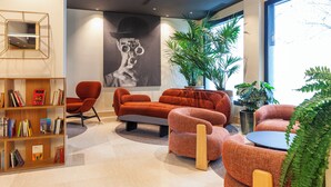 A modern interior with a sofa, armchairs, a bookshelf, and a large window. - Hotel SB Madrid Norte (San Sebastian de los Reyes)