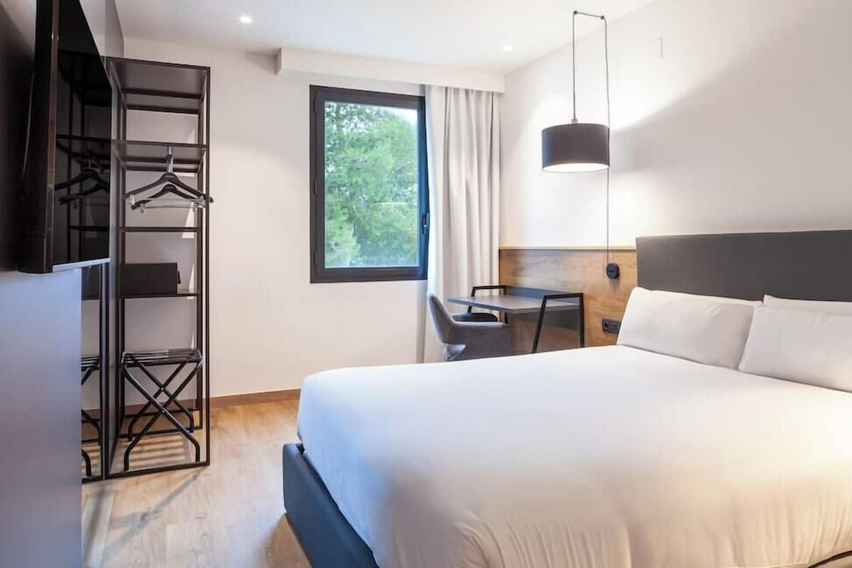Ein Hotelzimmer mit einem Bett, einem Schreibtisch, einem Stuhl, einem Kleiderschrank und einem Fenster.