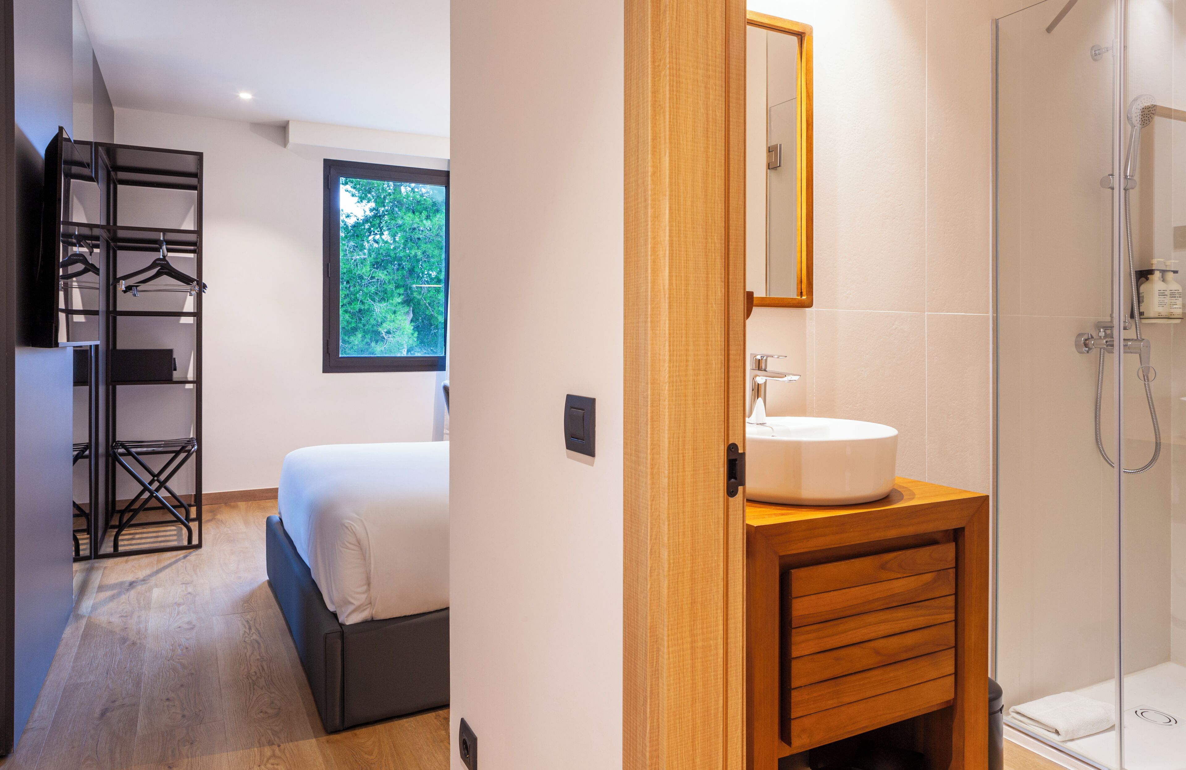 Una habitación de hotel moderna con cama, tocador de madera, ducha y armario empotrado.