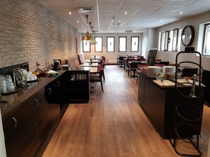 A modern cafe with brick walls, wooden flooring, and a central seating area with tables and chairs. - Hotell Stinsen (Hallsberg)
