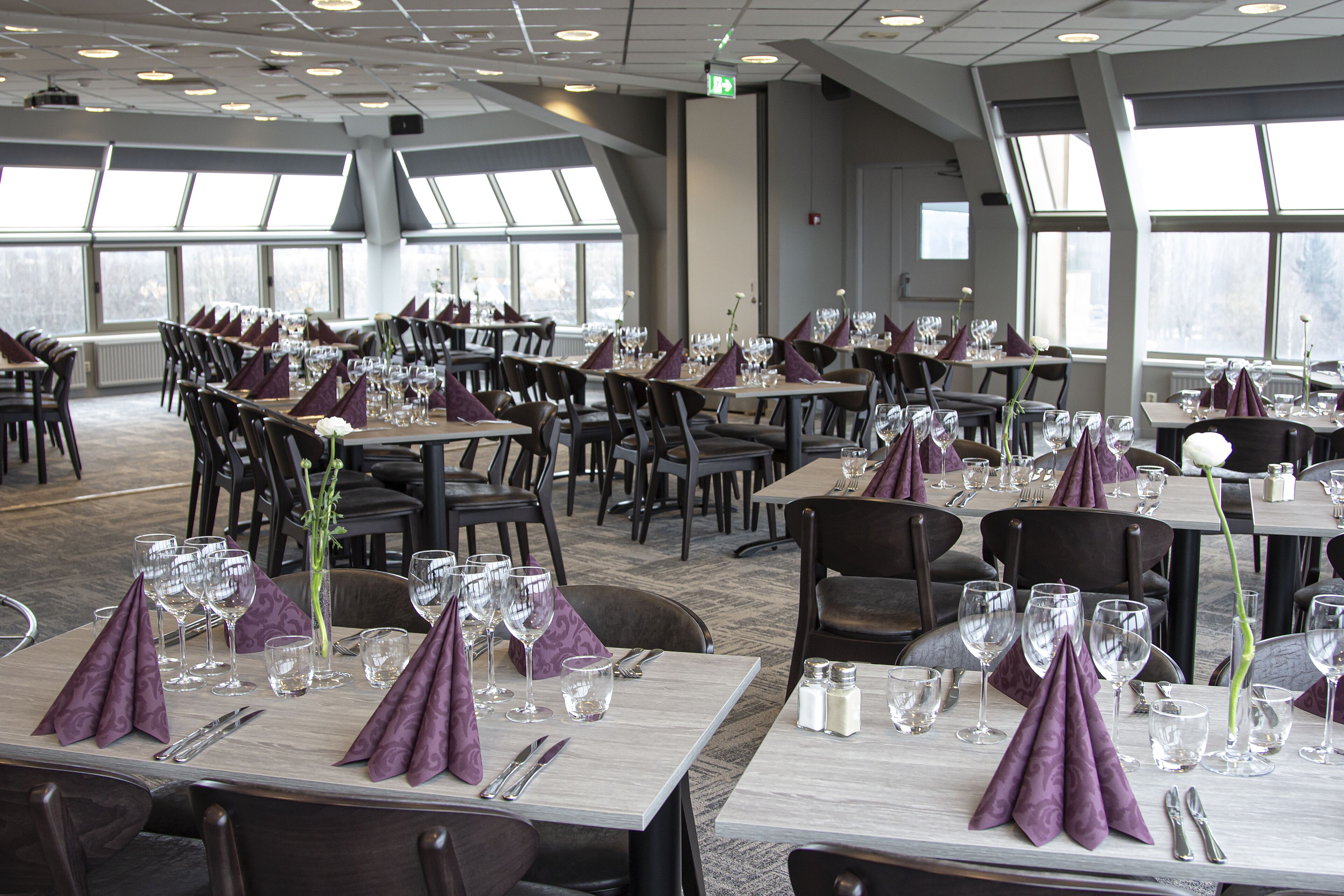 A restaurant with multiple tables set for dining, featuring purple napkins and clear glassware.