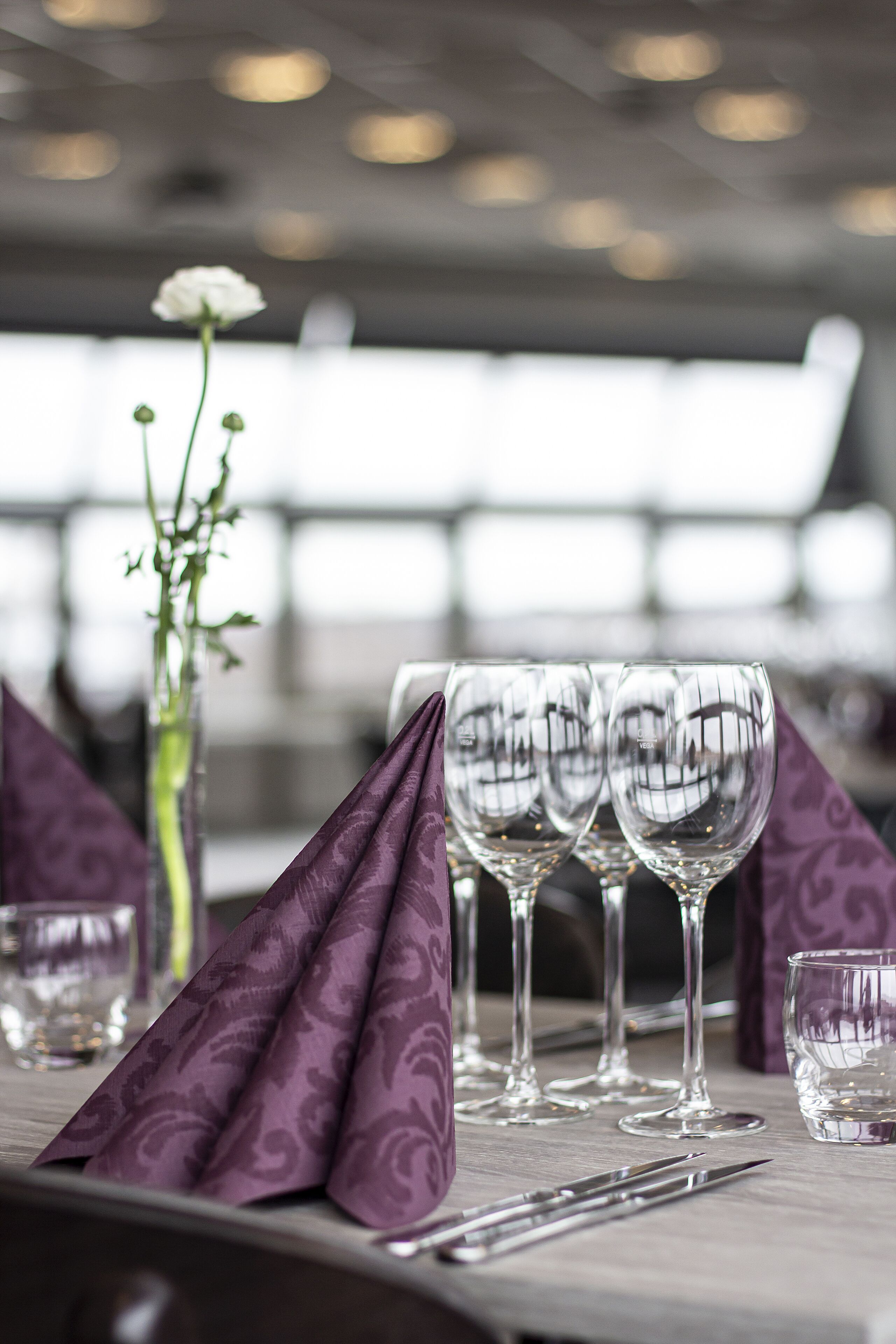 A table set with wine glasses and a vase with a single flower.