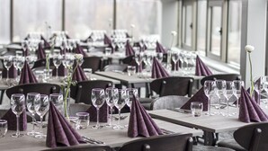 A restaurant with tables set with wine glasses and purple napkins, large windows, and a modern interior design. - Hotell Stinsen (Hallsberg)